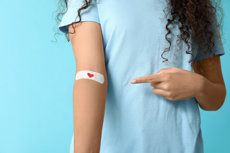 Young female African-American blood donor pointing at applied medical patch on blue backgroundの写真素材
