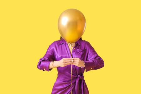 Young woman with air balloon on yellow backgroundの写真素材