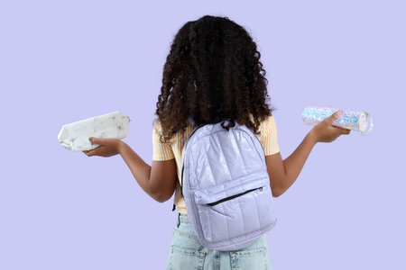 Little girl with pencil cases and backpack on lilac background, back view