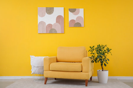 Interior of modern living room with cozy armchair, houseplant, pillow and pictures on yellow wallの写真素材