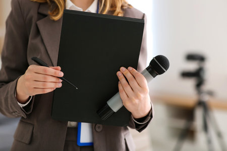 Beautiful young female reporter with microphone and notebook in office, closeupの写真素材