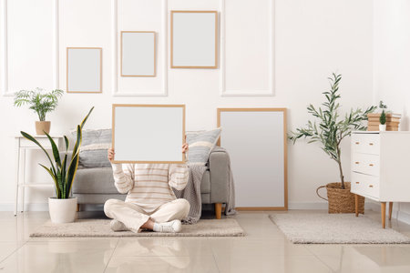 Young woman with blank frame sitting on floor in modern living room