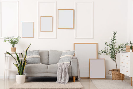 Interior of light living room with gray sofa, houseplants and blank framesの写真素材