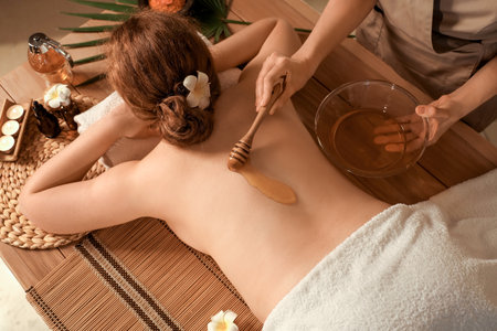 Massage therapist pouring honey on woman's back in dark spa salon, top viewの写真素材