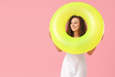 Beautiful young African-American woman with inflatable ring on pink background