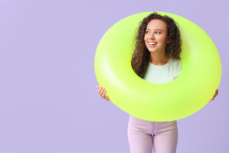 Beautiful young African-American woman with inflatable ring on lilac backgroundの写真素材