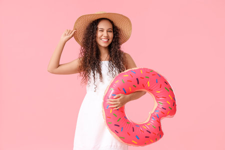 Beautiful young African-American woman with inflatable ring on pink backgroundの写真素材