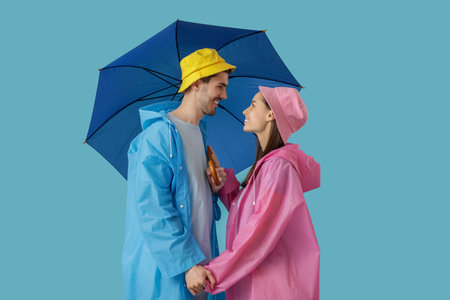 Young couple in raincoats with umbrella on blue backgroundの写真素材