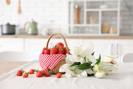 Wicker basket with tasty strawberries and lily flowers on table in kitchenの写真素材