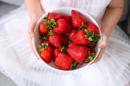 Little girl with bowl of delicious strawberries in living roomの写真素材