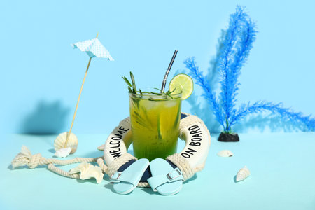 Glass of tasty cocktail with lifebuoy, shells, umbrella and flip flops on blue background