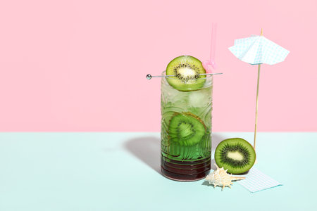 Glass of tasty cocktail with kiwi, shell and umbrella on colorful backgroundの写真素材