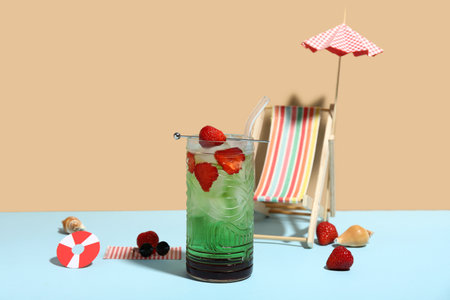 Glass of tasty cocktail with strawberry, shells, umbrella and deck chair on colorful backgroundの写真素材