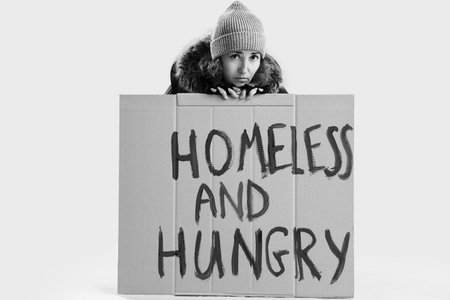 Mature woman behind cardboard with text HOMELESS AND HUNGRY on light backgroundの写真素材