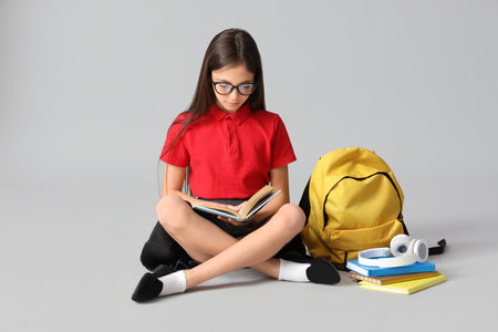 Little schoolgirl in eyeglasses reading book on light backgroundの写真素材