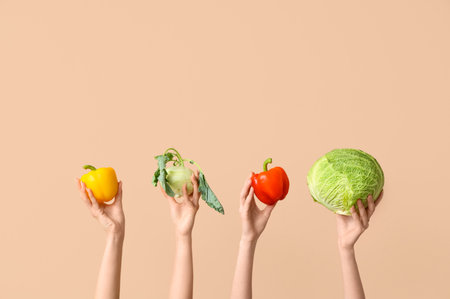 Female hands holding fresh vegetables on beige backgroundの写真素材