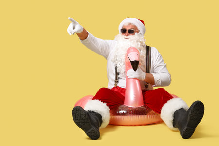 Santa Claus on swim ring pointing at something against yellow background. Christmas in Julyの写真素材
