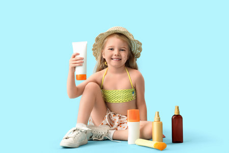 Cute little girl with bottles of sunscreen cream sitting on blue backgroundの写真素材