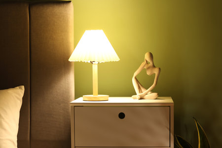Glowing lamp on bedside table near bed in bedroom, closeupの写真素材