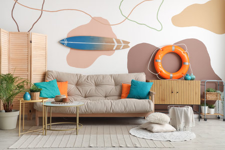 Stylish interior of living room with comfortable sofa, lifebuoy ring, coffee table and surfboardの写真素材