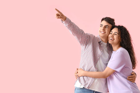 Young couple in love pointing at something on pink backgroundの写真素材