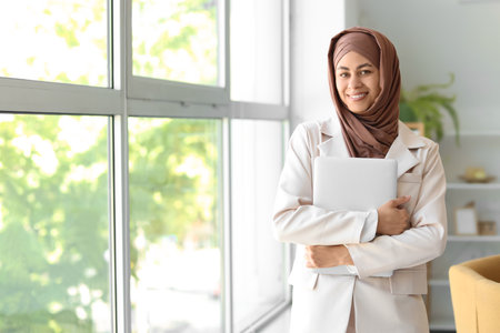 Muslim businesswoman with laptop near window at homeの写真素材