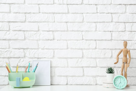 Modern workplace with alarm clock, stationery and mannequin near white brick wall in officeの写真素材