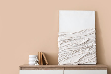 Picture and chest of drawers near beige wall in stylish room, closeup
