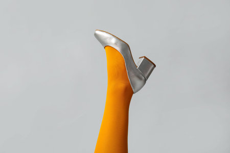 Leg of young woman in colorful tights and silver shoes on white background