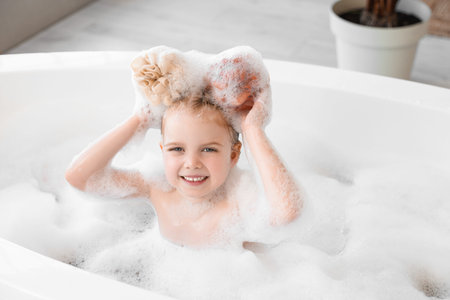 Cute little girl playing with bath sponges in bathtub