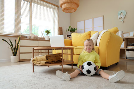 Cute little girl with soccer ball sitting on floor at homeの写真素材
