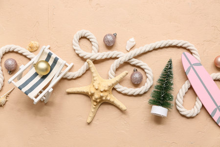 Tiny deck chair, starfish, toy surfboard and fir-tree with Christmas balls on beige background. Top...