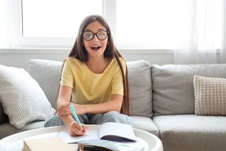 Happy little schoolgirl writing in copybook on sofa at homeの写真素材