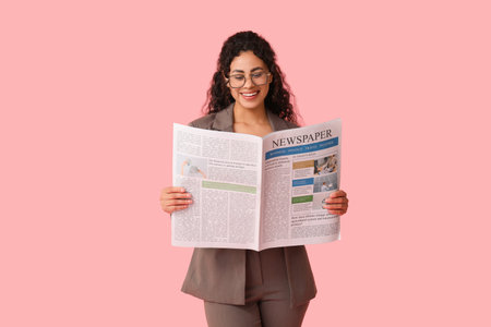 Beautiful young African-American woman reading newspaper on pink backgroundの写真素材