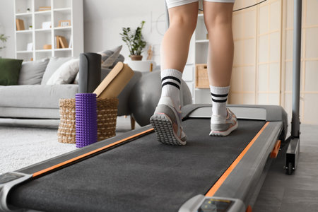 Sporty woman jogging on treadmill at home, back view