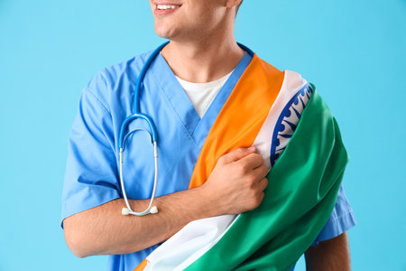 Male doctor with flag of India holding fist over heart on blue background. National Doctor's Day celebrationの写真素材