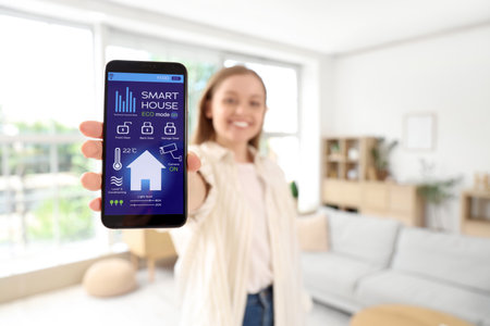 Young woman holding mobile phone with smart home security system control panel in room, closeupの写真素材