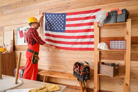 Male worker hanging USA flag on wall in workshop. Labor Day celebrationの写真素材