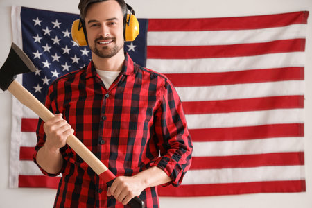Male worker with ax against USA flag on light background. Labor Day celebrationの写真素材