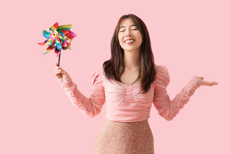 Young Asian woman with toy windmill on pink background