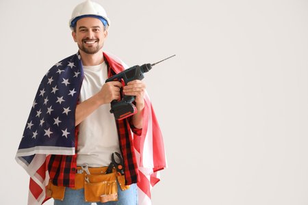 Male worker with USA flag and drill on light background. Labor Day celebrationの写真素材
