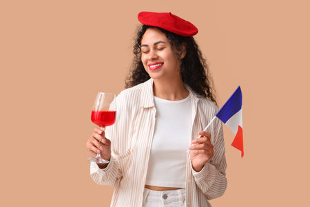 Beautiful young happy African-American woman with flag of France and glass of red wine on beige backgroundの写真素材