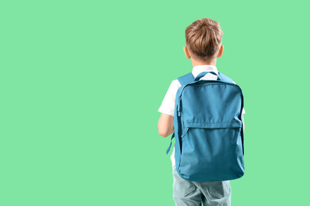Little schoolboy with blue backpack on green background, back viewの写真素材