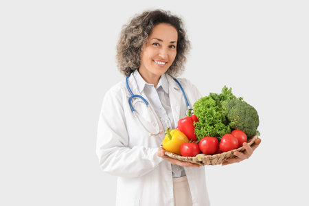 Mature female nutritionist with healthy vegetables on light backgroundの写真素材