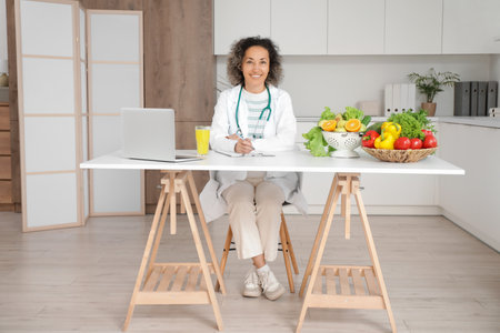 Mature female nutritionist sitting at table in kitchenの写真素材