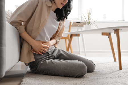 Young woman suffering from severe abdominal pain at home, closeupの写真素材