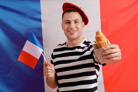 Young man in beret with croissant against flag of Franceの写真素材