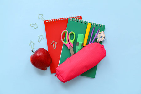 School supplies with notebooks, pencil case and red apple on blue background. Top view