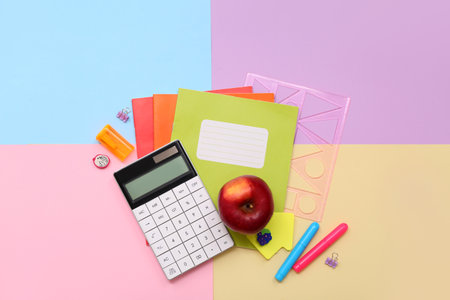 School supplies with calculator, red apple and copybooks on colorful background. Top viewの写真素材