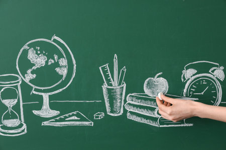 Female hand drawing school supplies on green chalkboardの写真素材